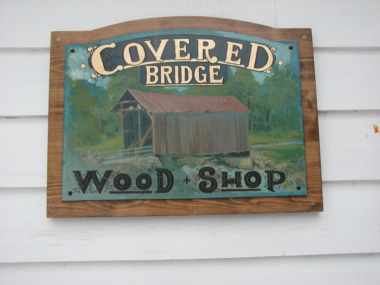 Hand-painted Covered Bridge Wood Shop sign on white siding